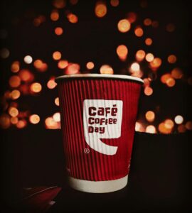 Red Cafe Coffee Day cup with bokeh background creates a warm and inviting atmosphere.
